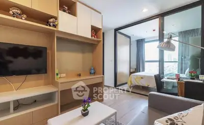 Modern living room with TV and view into cozy bedroom, featuring stylish decor and natural light.