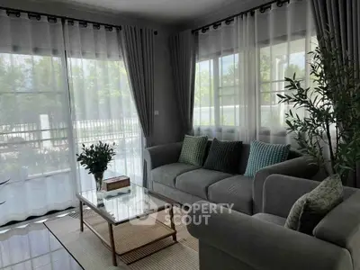 Elegant living room with large windows and modern decor, offering a serene garden view.