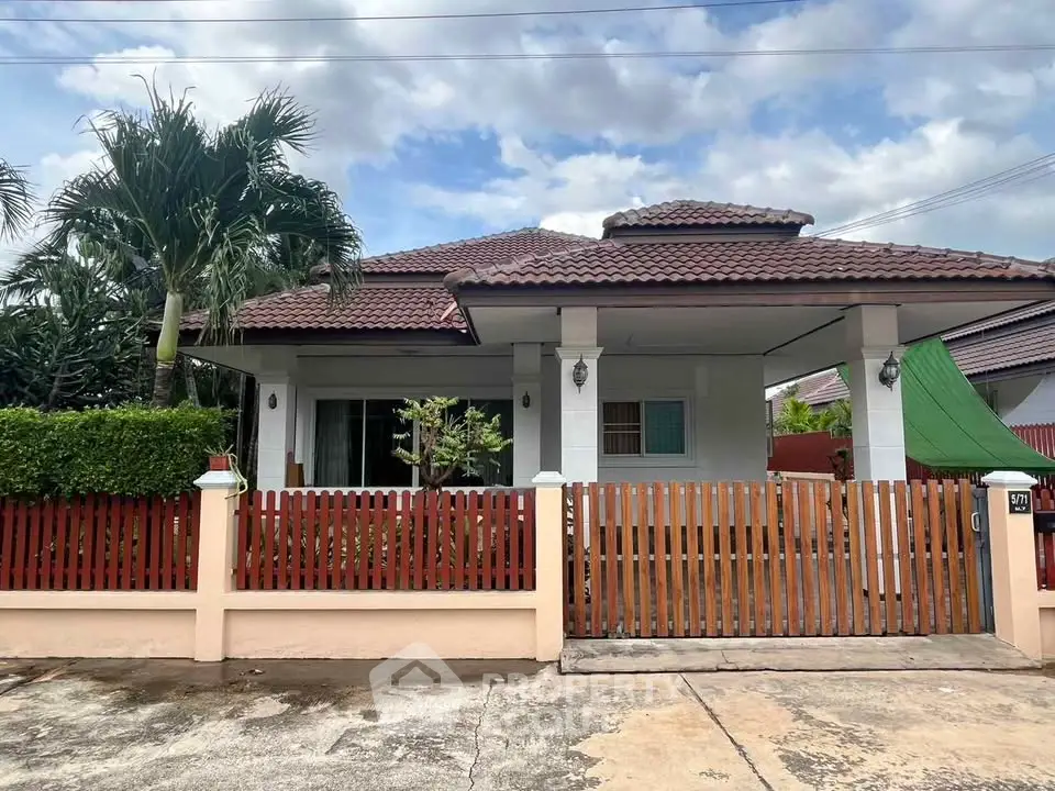 Charming single-story house with red-tiled roof and lush greenery in a serene neighborhood.