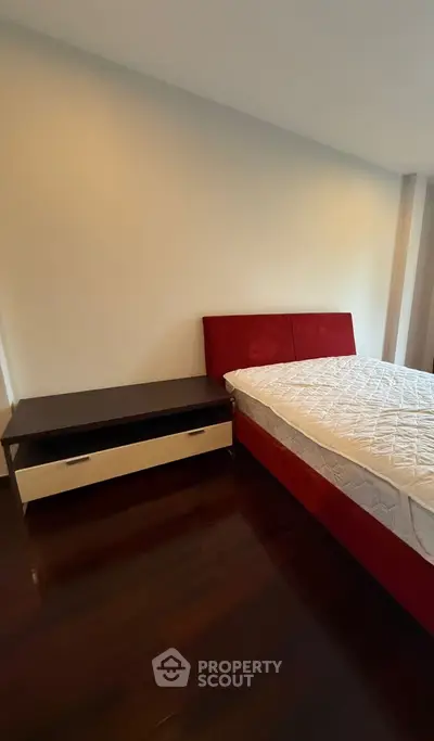 Spacious bedroom with elegant red bed and sleek wooden flooring.