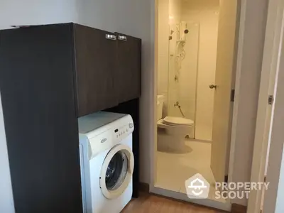 Compact modern bathroom with glass shower enclosure and adjacent laundry area featuring a front-loading washing machine and sleek cabinetry.