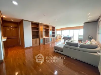 Spacious living room with wooden flooring and built-in shelves, featuring a cozy sofa and dining area with natural light.