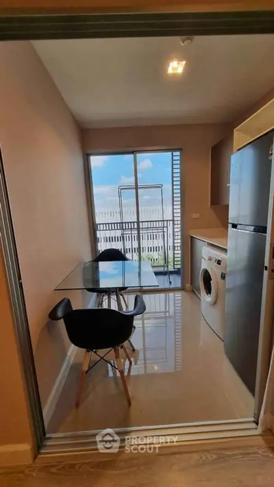 Modern kitchen with glass table, washing machine, and balcony view in urban apartment.