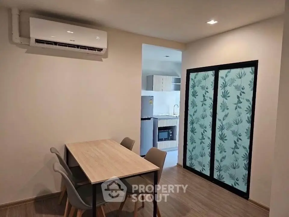 Modern dining area with air conditioning and view into a sleek kitchen with appliances.