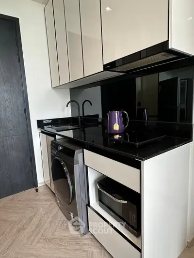 Modern kitchen with sleek cabinetry, black countertops, and built-in appliances including a washing machine.