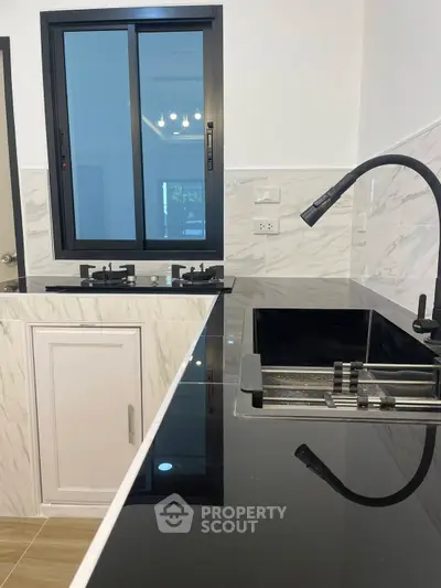 Modern kitchen with sleek black countertops and stylish fixtures, featuring a large window for natural light.