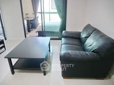 Modern living room with sleek black leather sofa and glass coffee table, adjacent to a cozy bedroom.