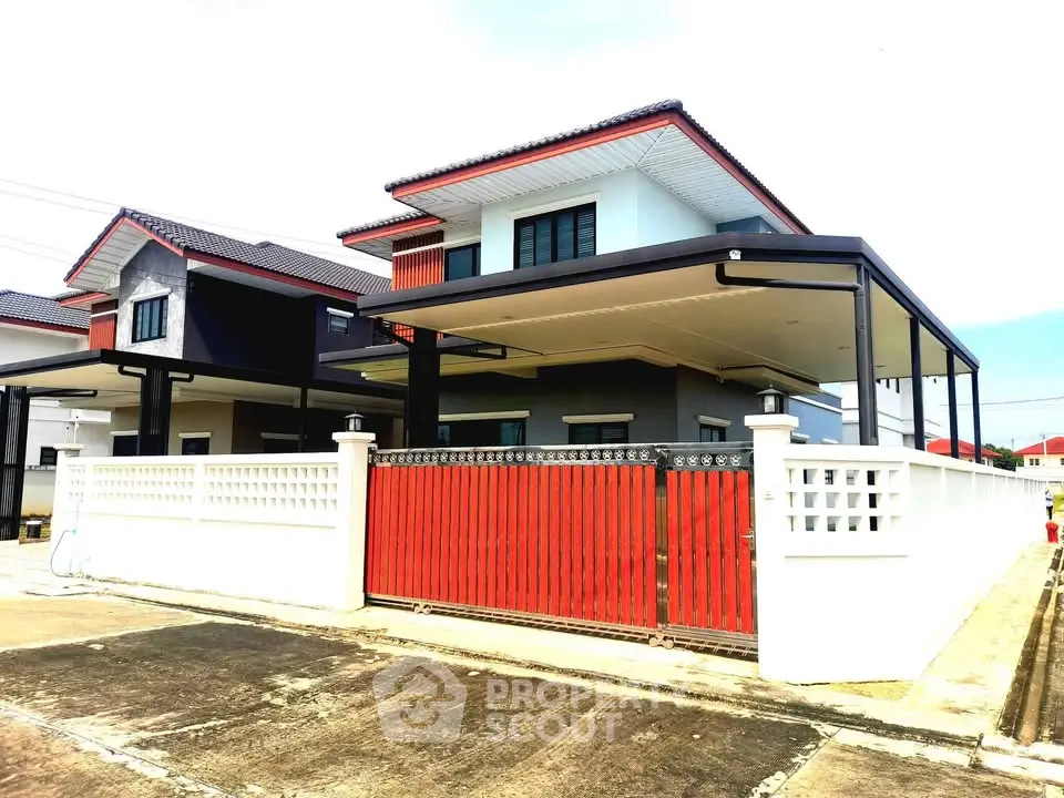 Modern two-story house with red accents and gated entrance in a suburban neighborhood.