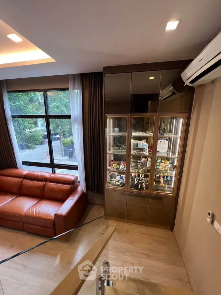 Stylish living room with large window, leather sofa, and display cabinet in modern home.