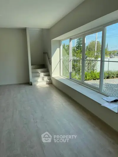 Spacious room with large window and staircase, offering natural light and outdoor view.