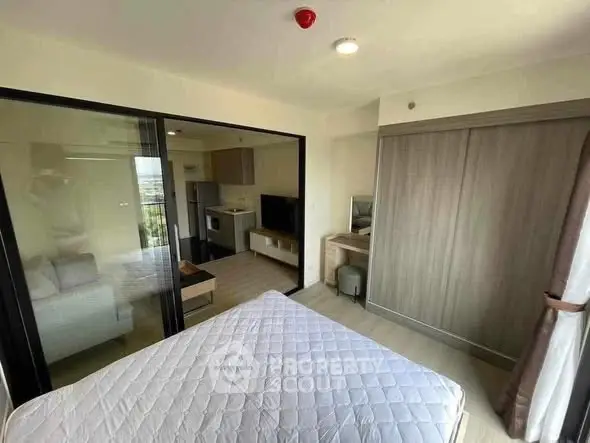 Modern apartment bedroom with sliding glass doors and compact kitchen view.