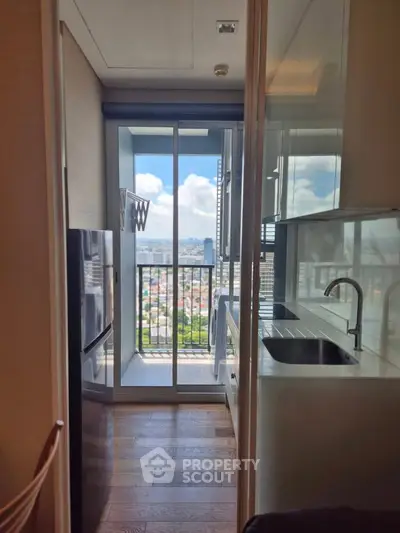 Modern kitchen with balcony view in high-rise apartment, featuring sleek cabinetry and wooden flooring.