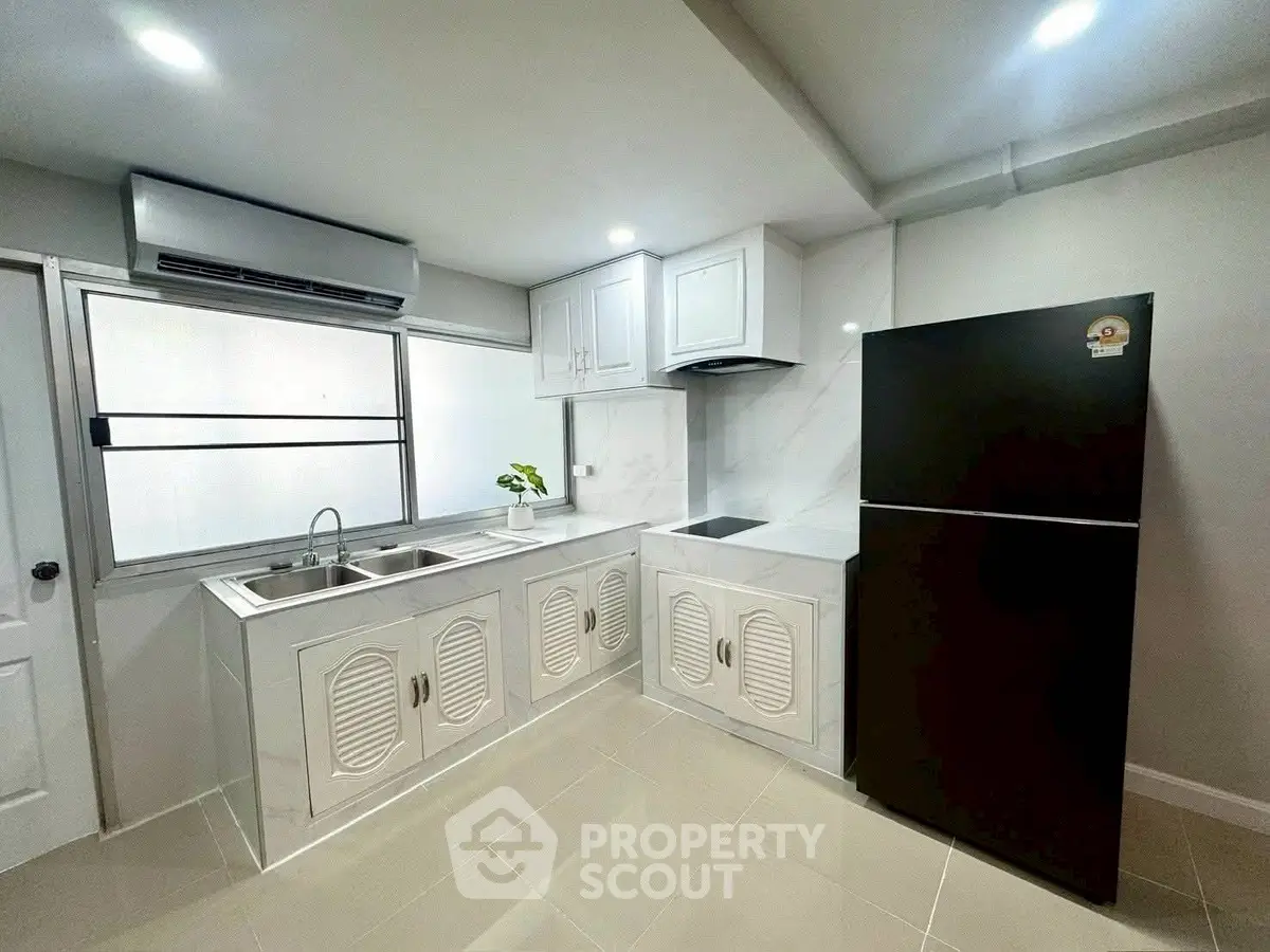 Modern kitchen with sleek white cabinetry and black refrigerator, featuring a minimalist design and ample natural light.