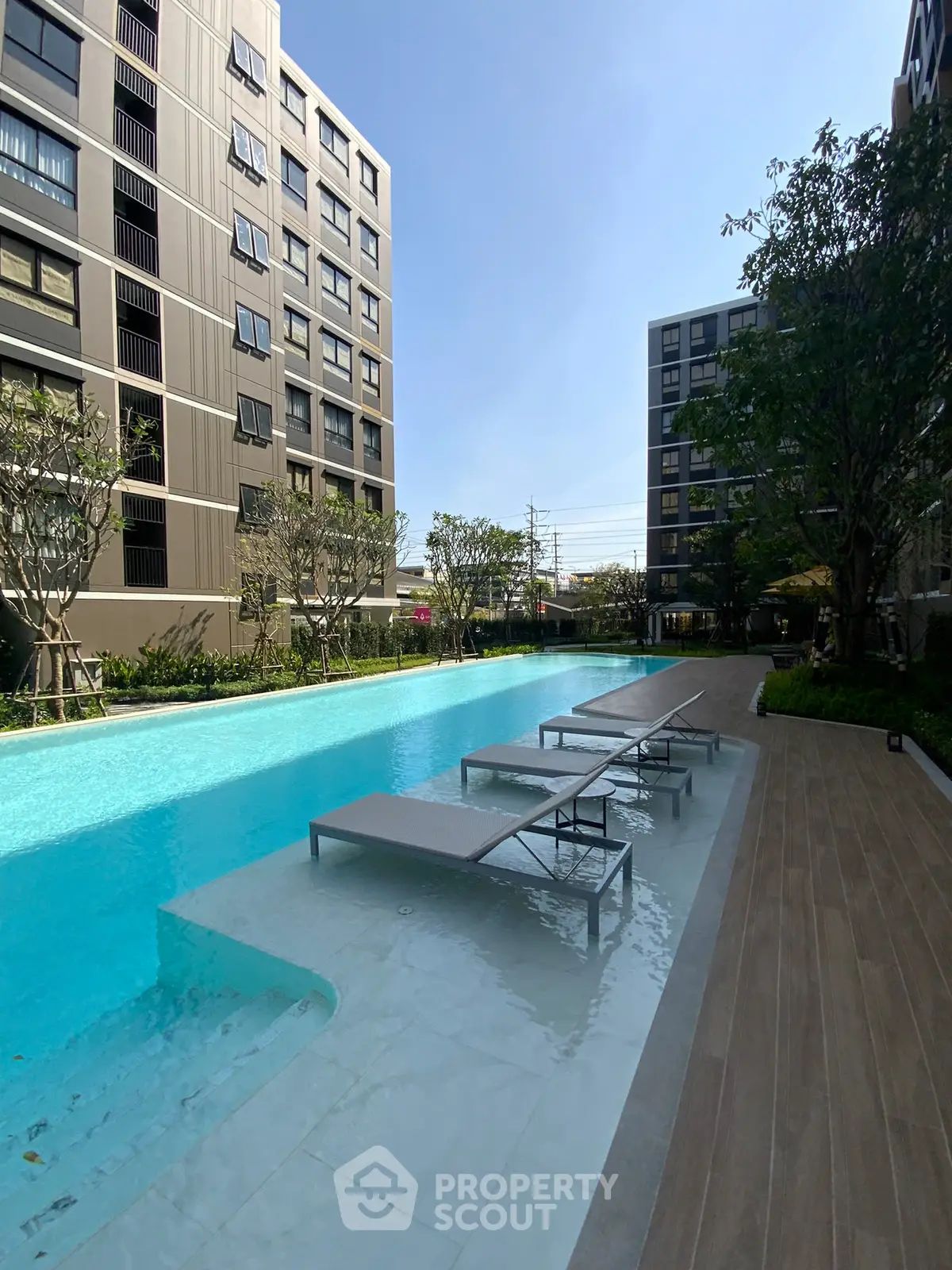 Luxurious modern apartment complex with stunning poolside view and sun loungers.