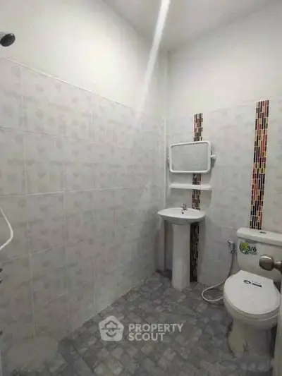 Compact bathroom with tiled walls and floor, featuring a toilet and pedestal sink.