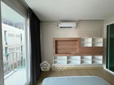 Modern bedroom with built-in shelving and air conditioning, featuring a large window with balcony access.