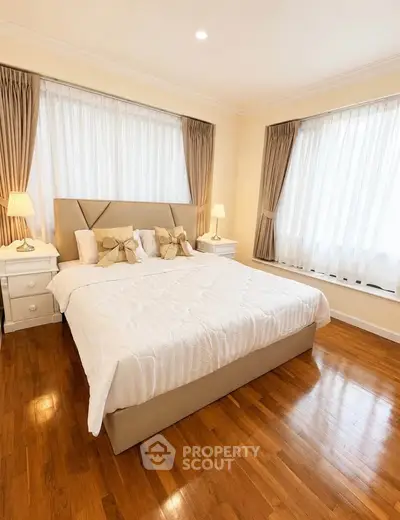 Elegant bedroom with hardwood floors and large windows in a cozy real estate property.