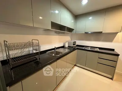 Modern kitchen with sleek cabinetry and black countertops, featuring a gas stove and microwave.