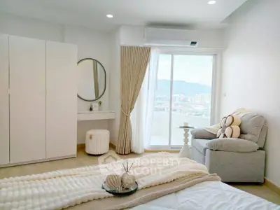 Bright and cozy bedroom with balcony and stunning city view, featuring modern decor and comfortable seating.