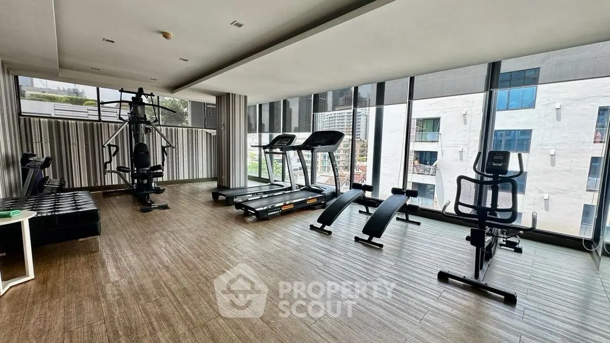 Spacious modern gym with large windows and fitness equipment in luxury building.