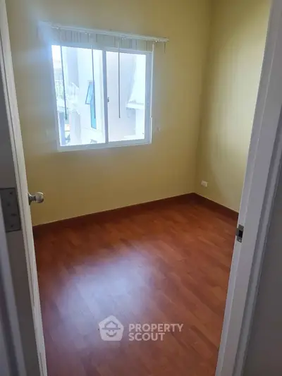 Cozy empty bedroom with wooden flooring and large window for natural light.