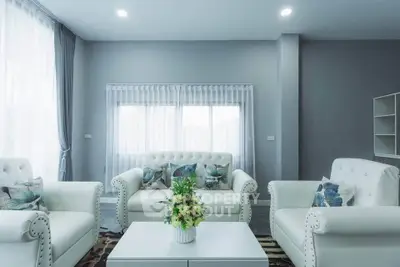 Elegant living room with plush white sofas and floral cushions, featuring large windows and soft lighting.