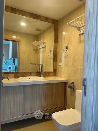 Modern bathroom with sleek fixtures and wooden cabinetry, featuring a large mirror and elegant lighting.