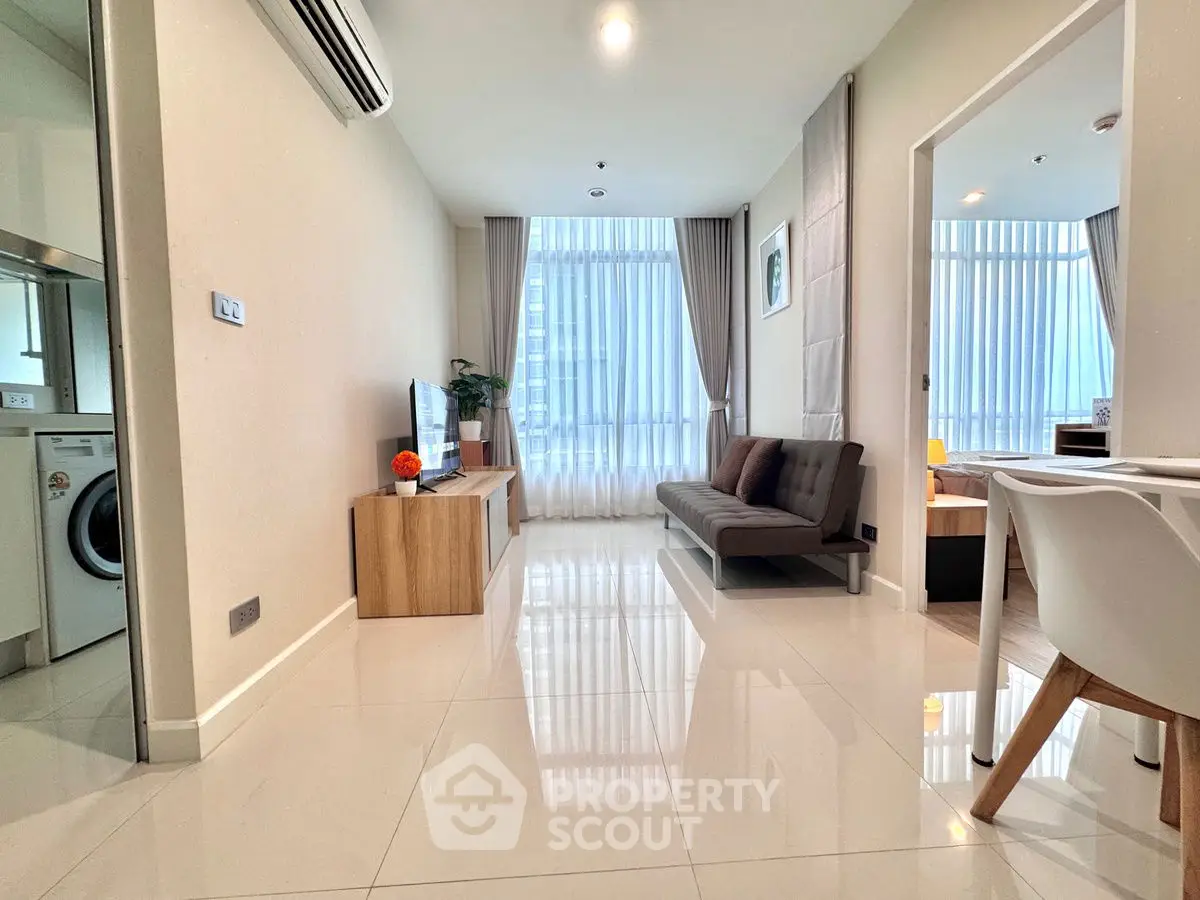Modern living room with sleek furniture and natural light, adjacent to a compact kitchen area.