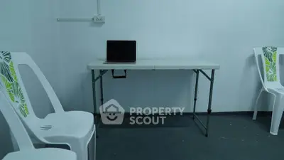 Minimalist room with white plastic chairs and a simple table with a laptop.