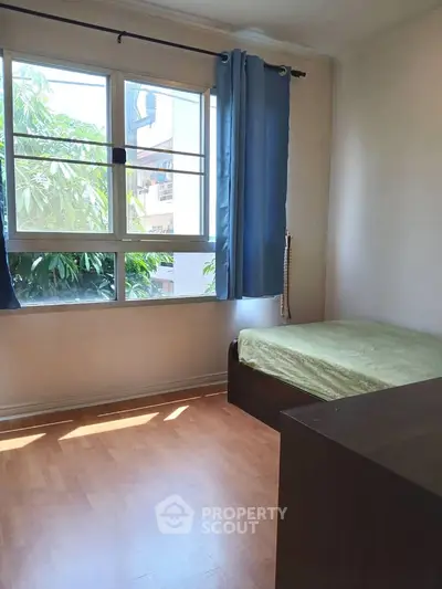 Cozy bedroom with large window and natural light, featuring a single bed and wooden flooring.