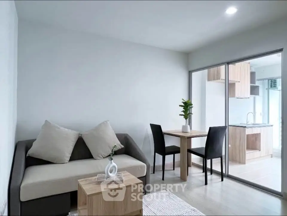 Modern living room with open kitchen, featuring sleek furniture and bright natural lighting.