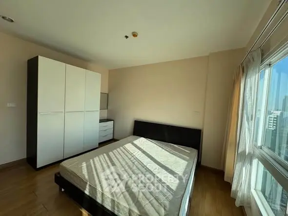 Spacious bedroom with large window and modern wardrobe in bright apartment.