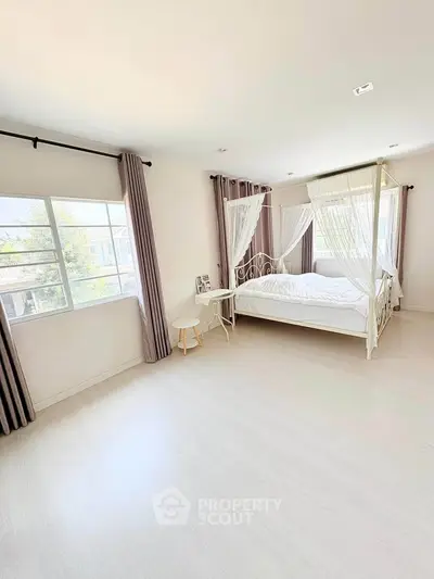 Spacious and bright bedroom with elegant canopy bed and large windows in modern home.