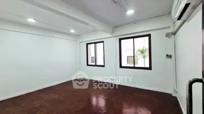 Spacious and well-lit corner unit with polished brown flooring and white walls, featuring large windows and modern air conditioning.