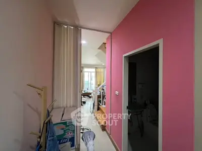 Cozy hallway leading to a bright living area with pink accent wall and modern decor.