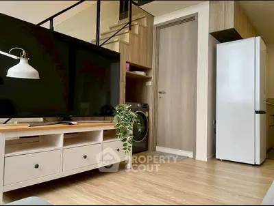Modern living room with TV, washing machine, and sleek refrigerator in stylish apartment.