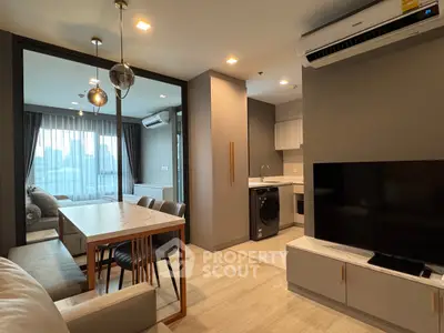 Modern open-plan living room with dining area and kitchen, featuring sleek furniture and large windows.