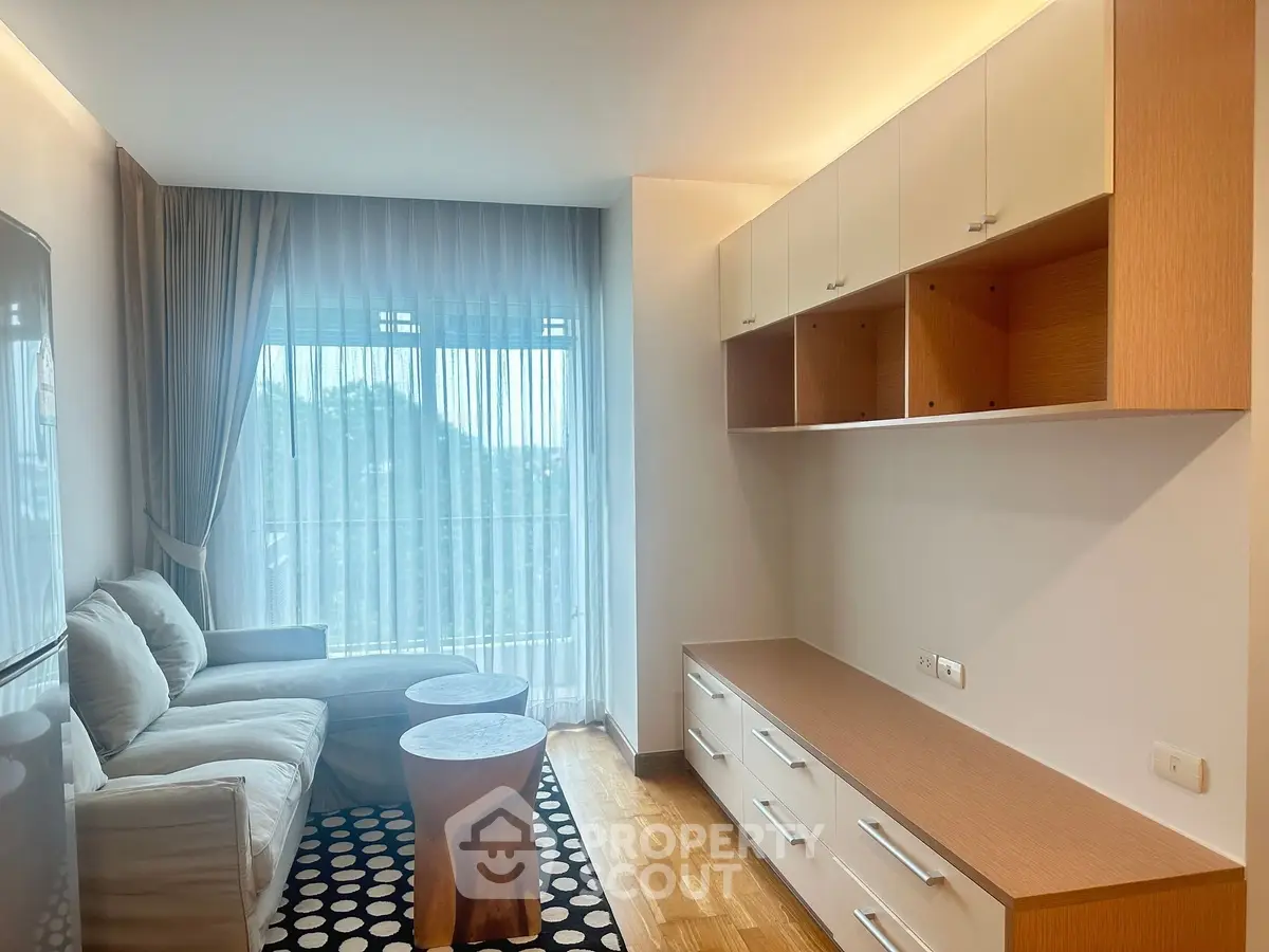 Modern living room with cozy sofa, stylish wooden cabinets, and large window with sheer curtains.