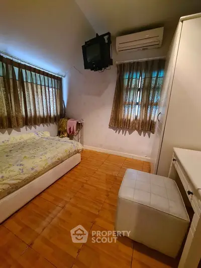 Cozy bedroom with wooden flooring, air conditioning, and natural light from two windows.