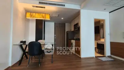 Modern apartment interior with dining area and kitchen featuring wooden flooring and stylish lighting.