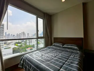 Cozy bedroom with large window offering stunning city view, perfect for urban living.