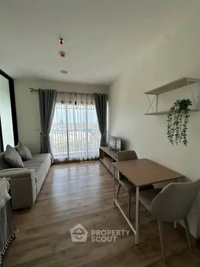 Modern living room with large window and city view, featuring cozy seating and dining area.