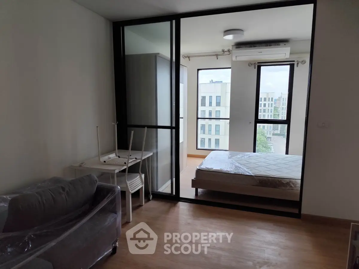 Modern apartment interior with bedroom and living area, featuring large windows and natural light.