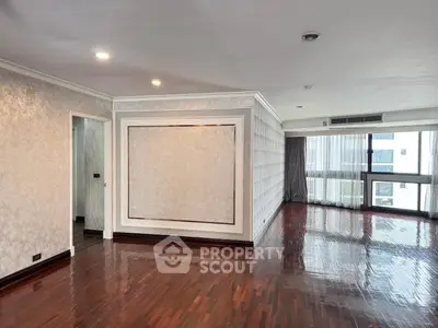 Spacious empty living room with polished wooden floors and large windows in a modern apartment.