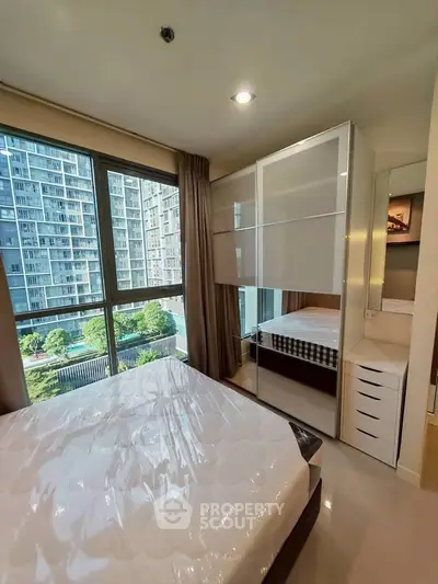 Modern bedroom with large window offering city view, featuring sleek furniture and natural light.