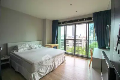 Spacious bedroom with large window offering city view and natural light, featuring modern furnishings.
