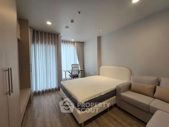 Modern bedroom with cozy bed, stylish sofa, and work desk near large window.