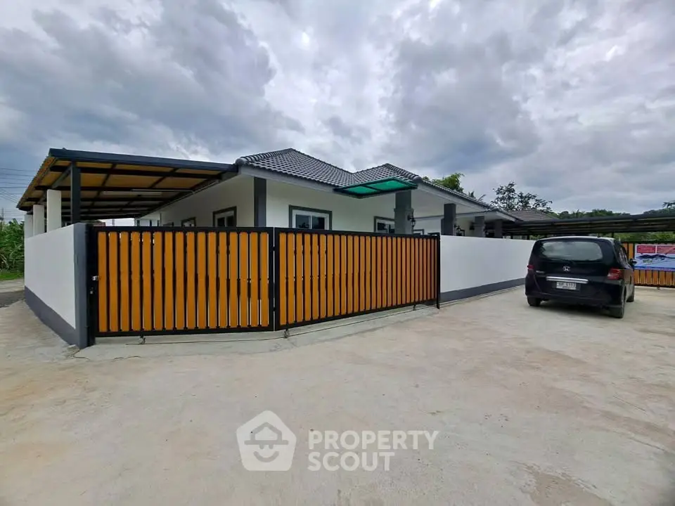 Modern single-story house with gated driveway and carport under cloudy sky.