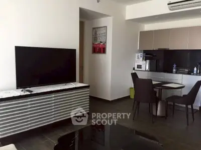 Modern living room with sleek furniture and integrated kitchen area, featuring a large flat-screen TV and dining set.