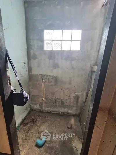 Unfinished bathroom space with concrete walls and small window, potential for renovation.